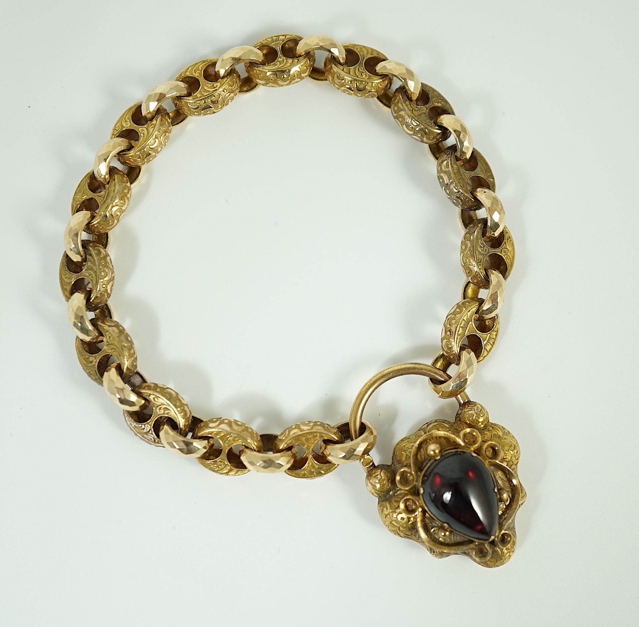 A Victorian engraved and facetted link gold mourning bracelet, with pear shaped foil backed? garnet set heart shape padlock